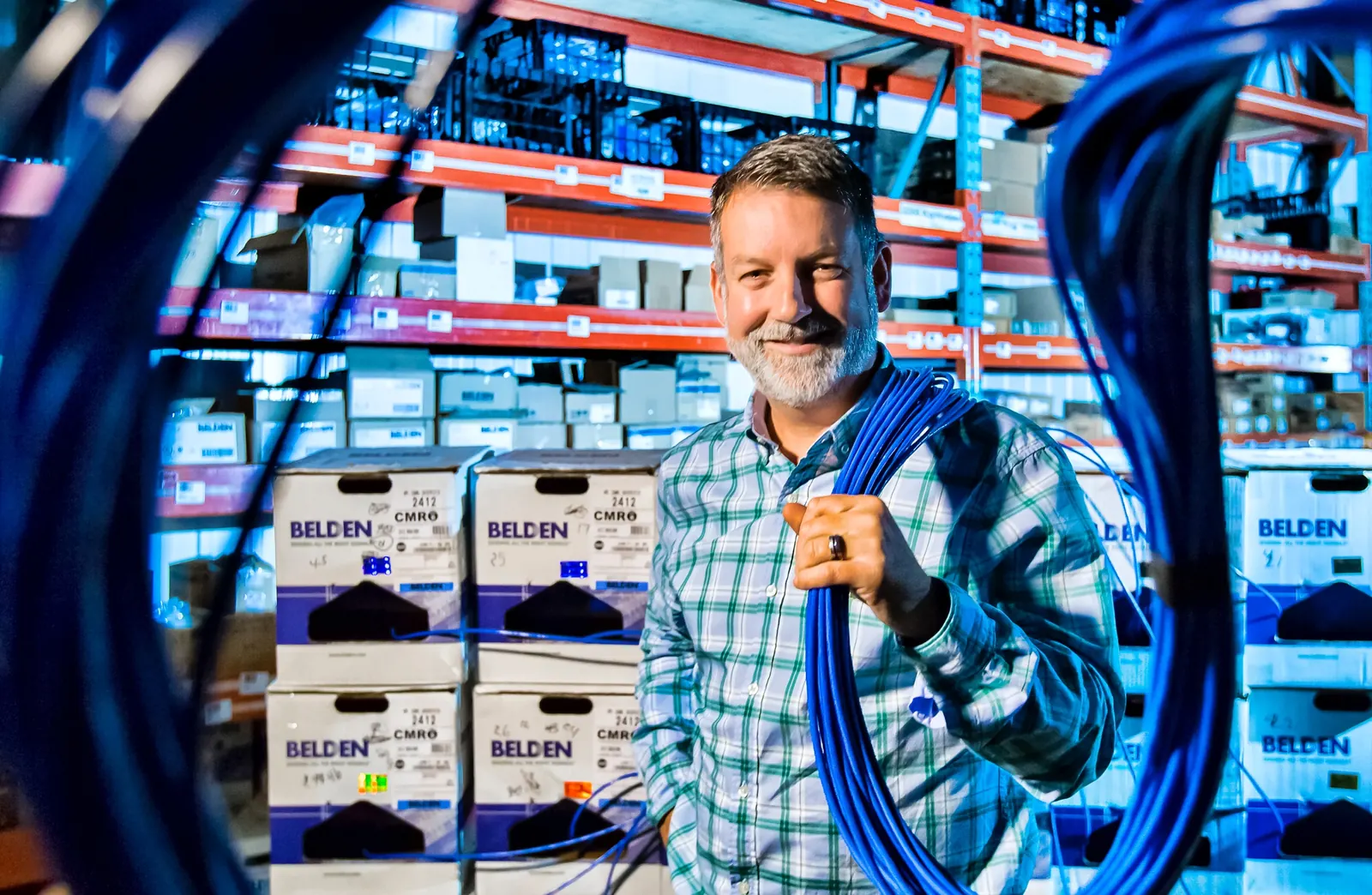 Membre de l’équipe LP Télécom tenant un rouleau de câble devant des boîtes de câbles Belden